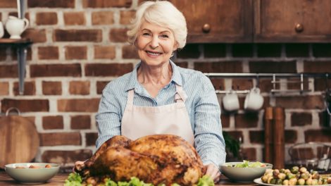 szép idős hölgy a konyhában egy egész grillcsirkével