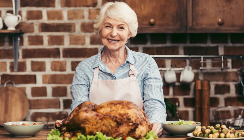 szép idős hölgy a konyhában egy egész grillcsirkével