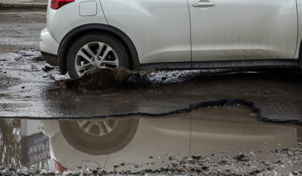 autó hajt bele a kátyúba