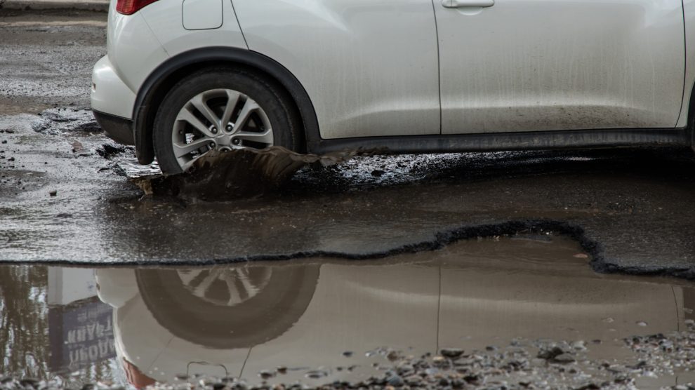 autó hajt bele a kátyúba