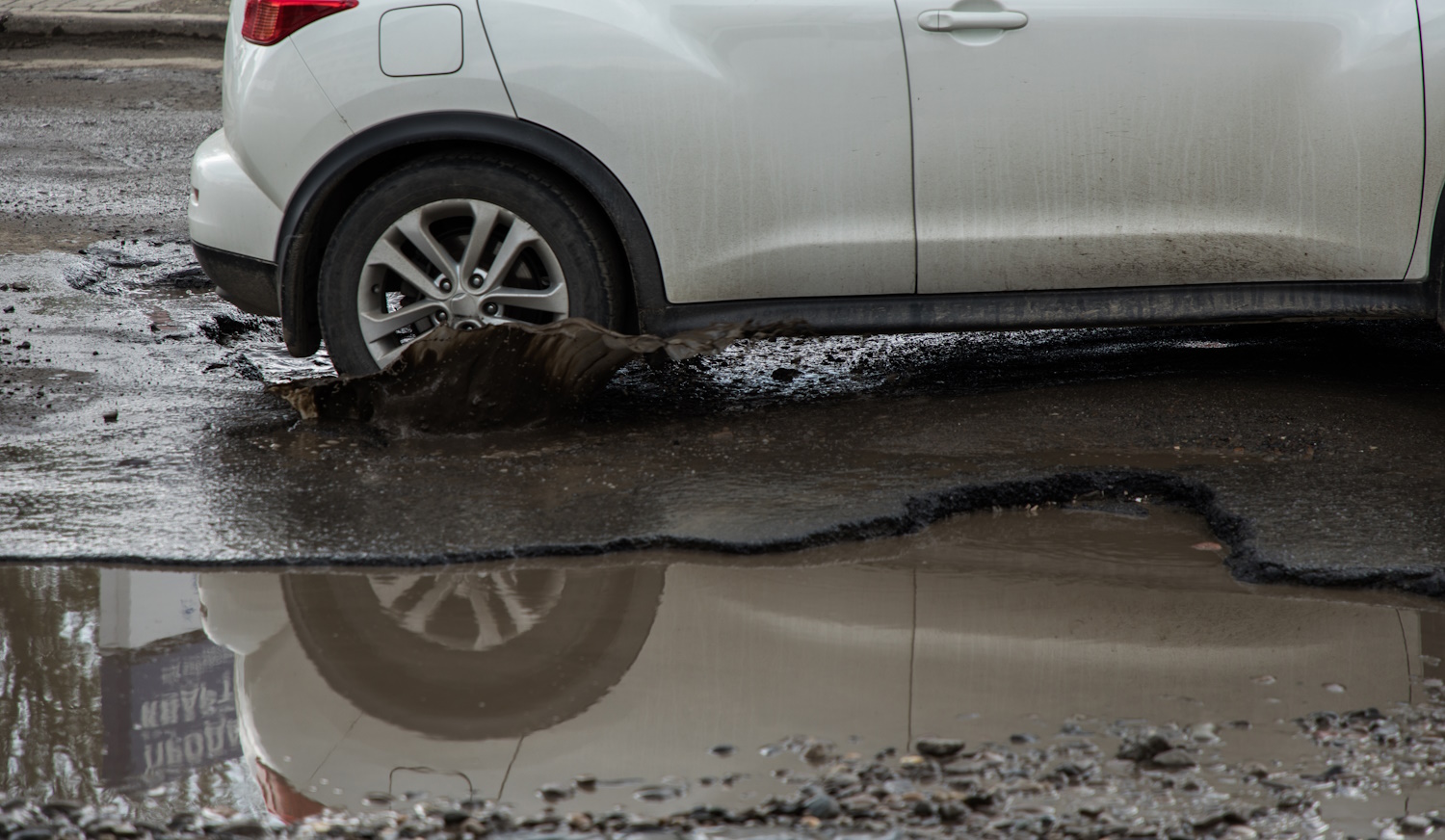 autó hajt bele a kátyúba