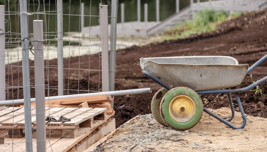 kiásott kerítés alap mellett talicska áll