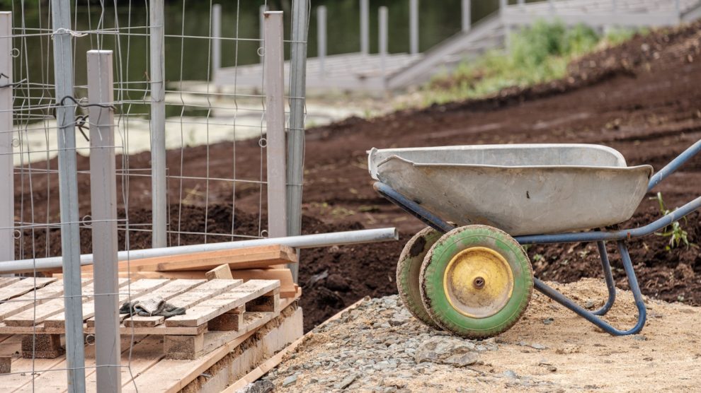 kiásott kerítés alap mellett talicska áll