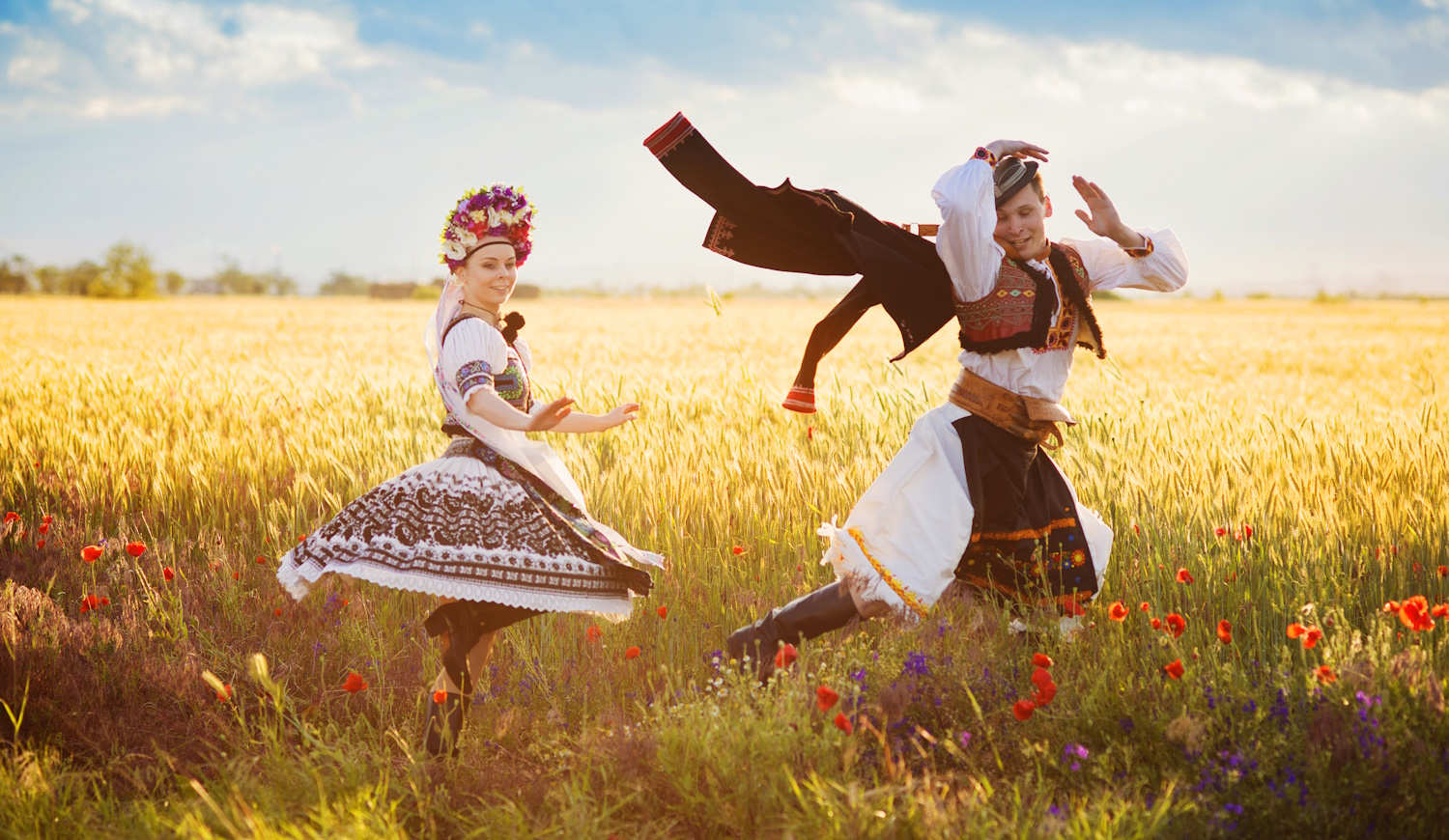 magyar népviseletbe öltözött fiata pár táncol a búzamezőn