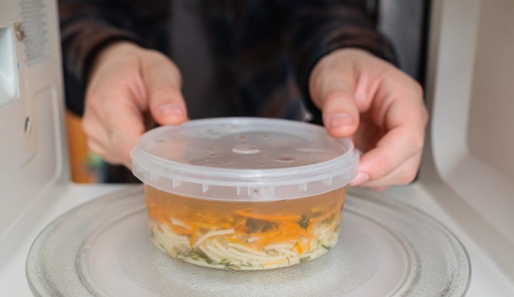 műanyag dobozban húslevest tesz a mikróba egy férfi