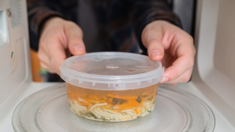 műanyag dobozban húslevest tesz a mikróba egy férfi