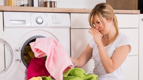 nő szedi ki a mosógépből a büdös ruhákat