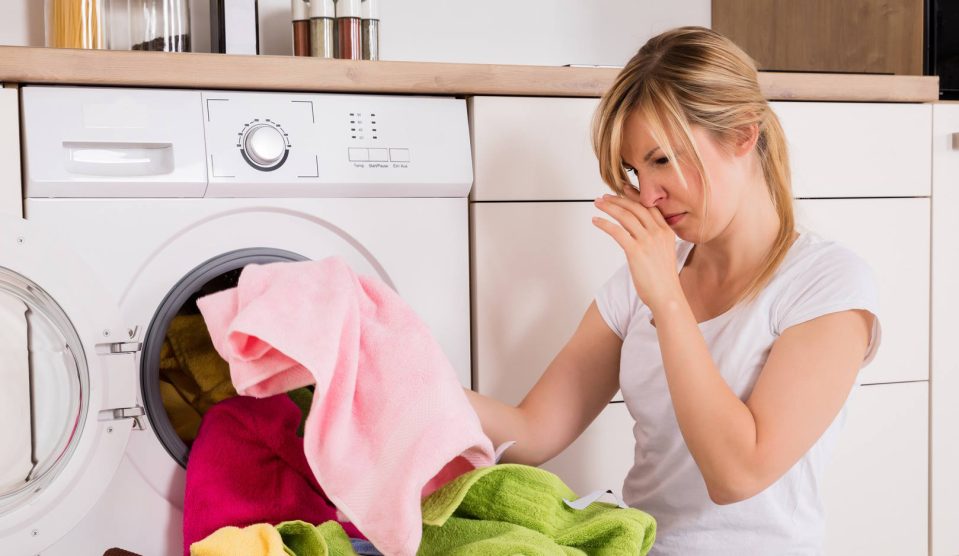 nő szedi ki a mosógépből a büdös ruhákat