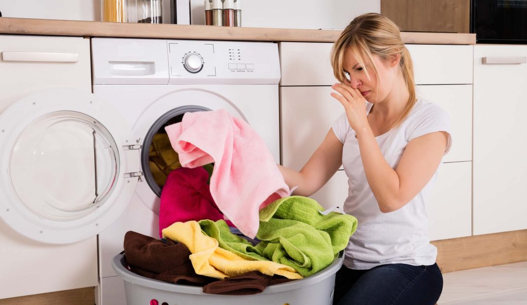 Fiatal nő szedi ki a frissen mosott büdös ruhákat a mosógépből