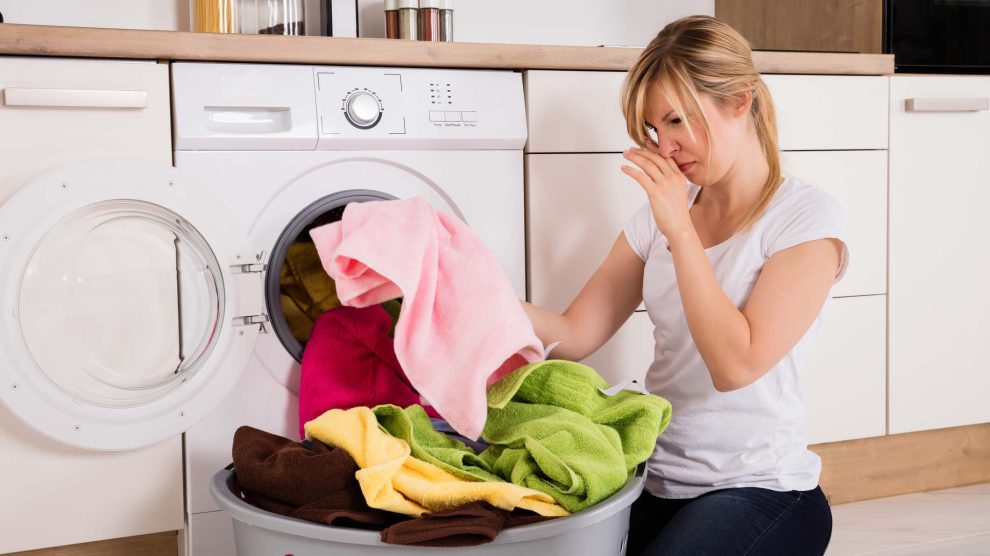 Fiatal nő szedi ki a frissen mosott büdös ruhákat a mosógépből