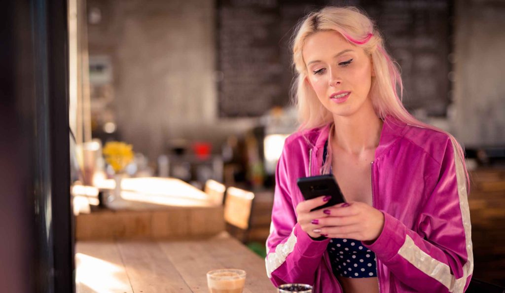 fiatal nő kávézás közben a telefonját nyomkodja