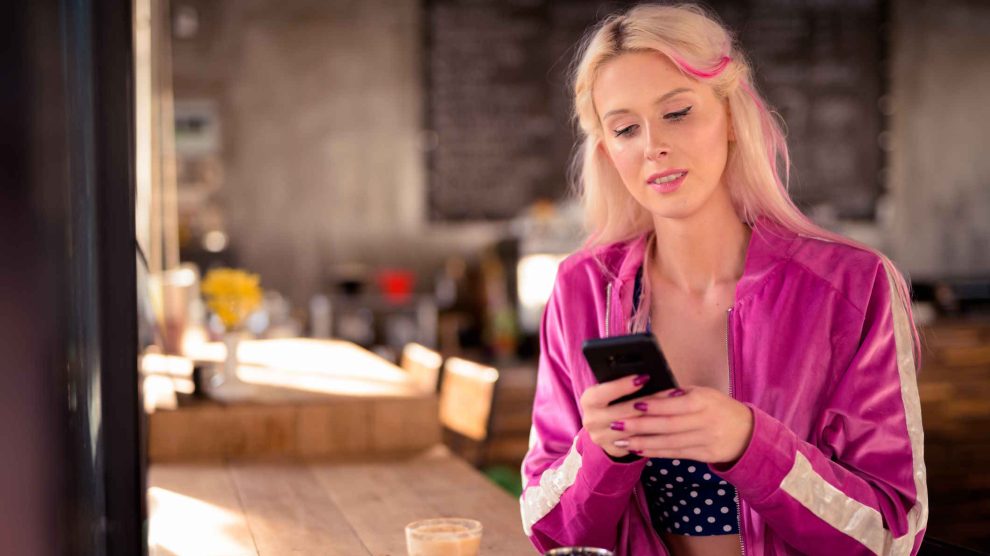 fiatal nő kávézás közben a telefonját nyomkodja