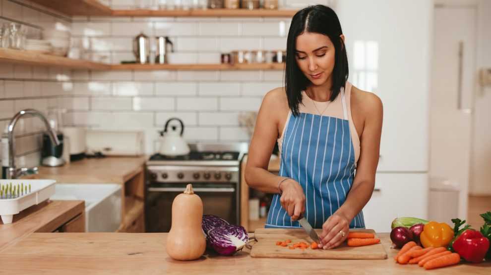 fa vágódeszkén zöldséget aprít egy fiatal háziasszony