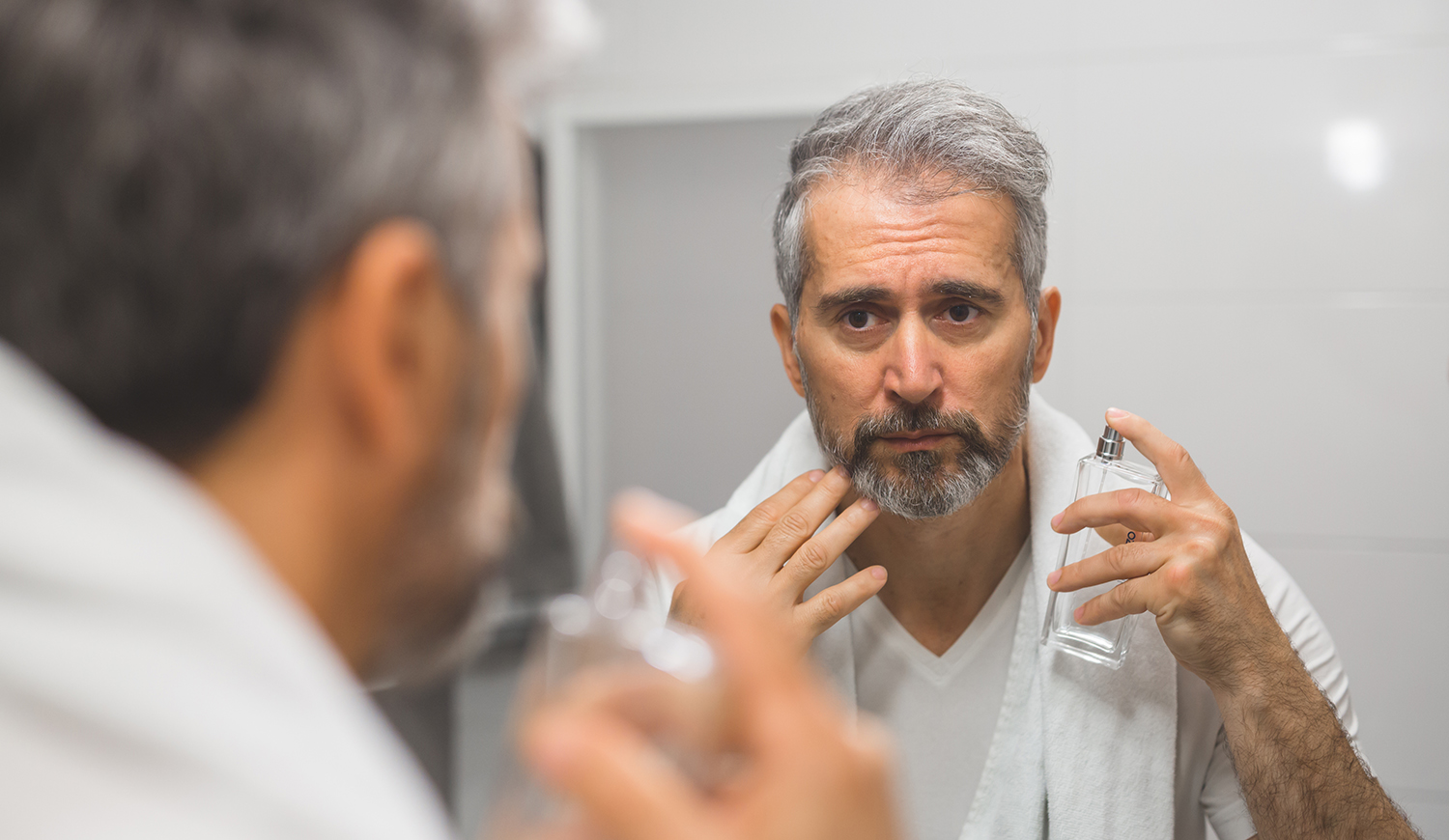 Középkorú szakállas, ősz hajú férfi parfümöt fúj magára