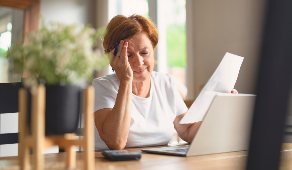 aggódó nyugdíjas hölgy a számlái fölött bosszankodik