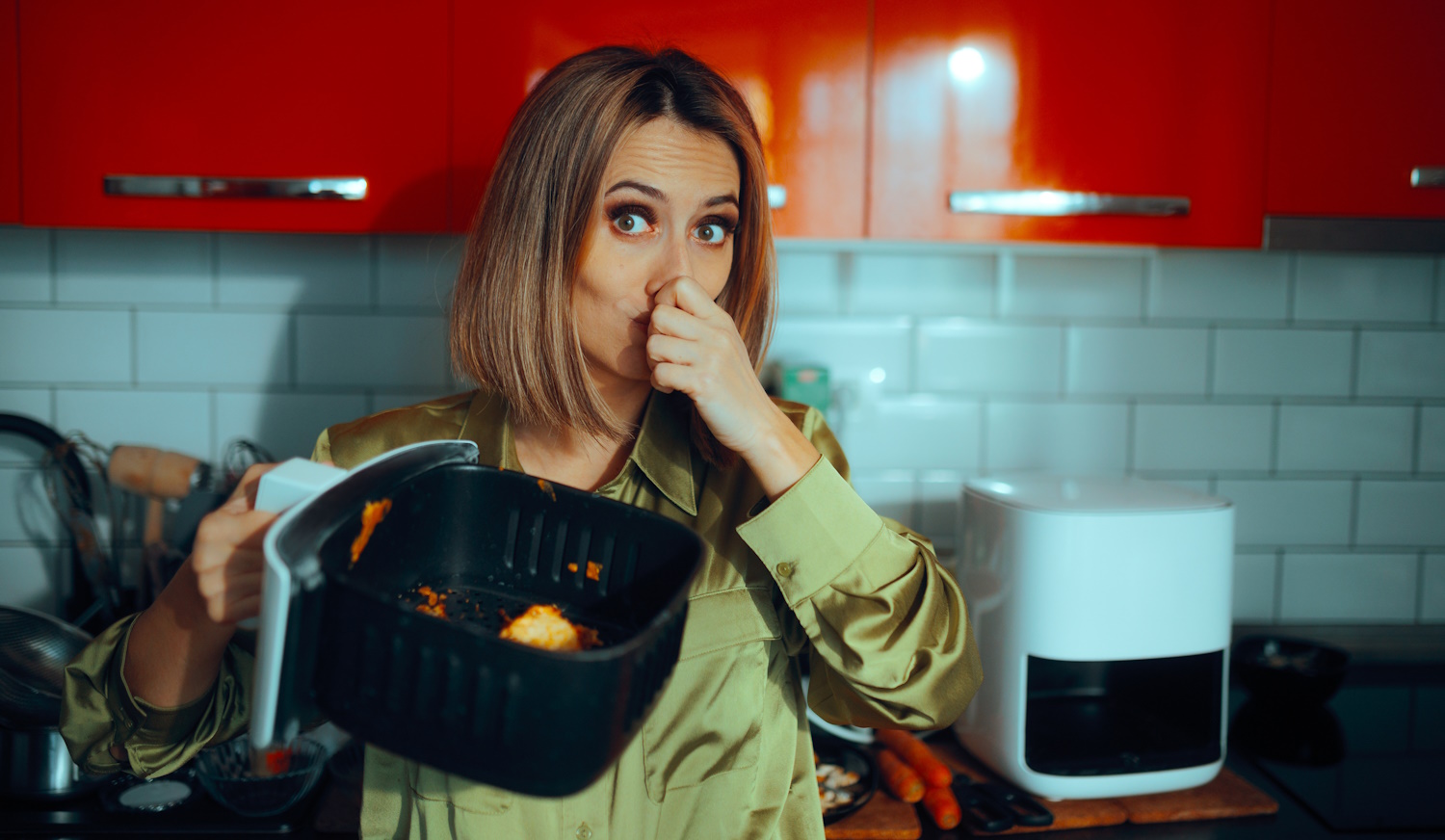„Egy nő undorodva befogja az orrát, miközben egy szennyezett airfryer kosarat tart. A készülékben maradt ételmaradékok kellemetlen szagot árasztanak.”