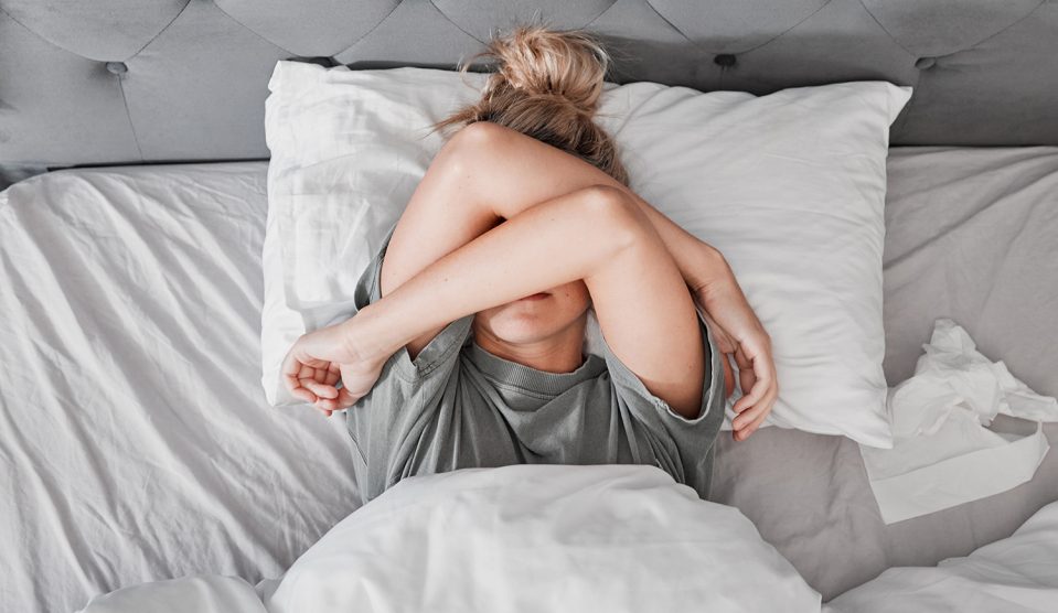 Fárad nő fekszi az ágyban, karjait a szeme elé téve