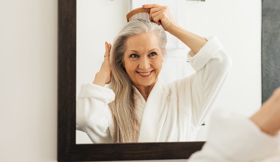 Mosolygó idős nő fésülködik fürdőszobai tükör előtt