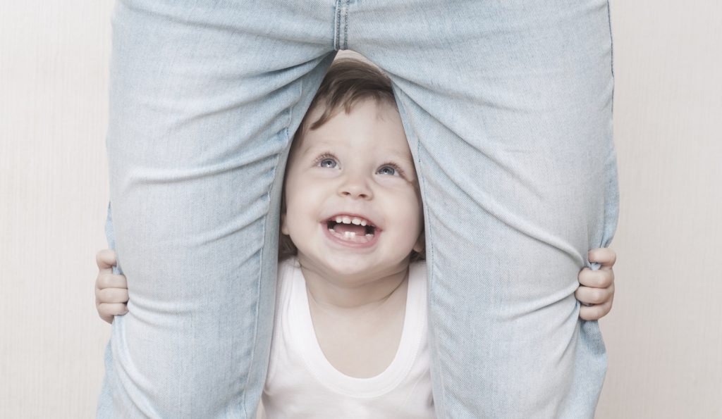 kacagó kisfiú áll az anyukája lába között