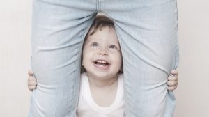 kacagó kisfiú áll az anyukája lába között