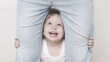 kacagó kisfiú áll az anyukája lába között