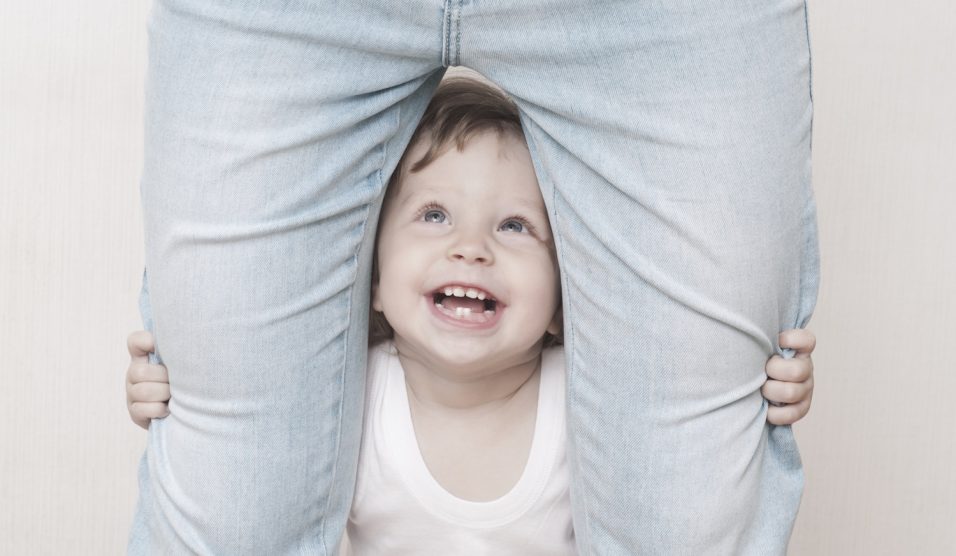 kacagó kisfiú áll az anyukája lába között