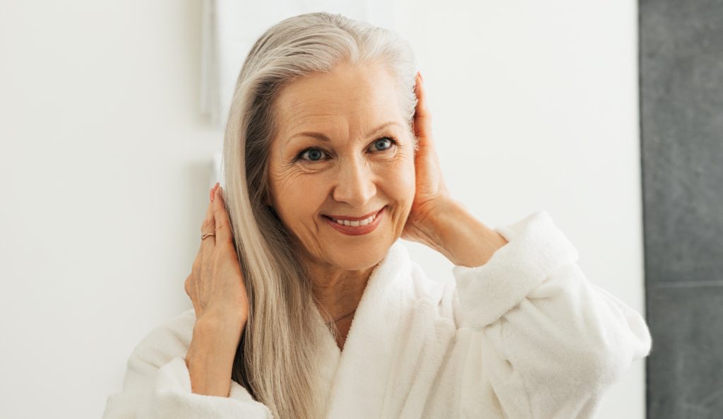 60 év feletti szép idős nő a fördőszobában a szép dús haját nézi a tükörben