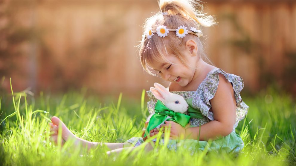 húsvéti nyuszit ölelget egy cuki szőke kislány a fűben