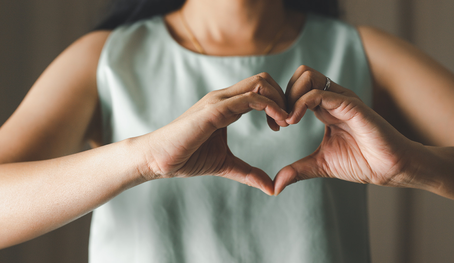 Szív alakot formáz a kezeivel egy nő