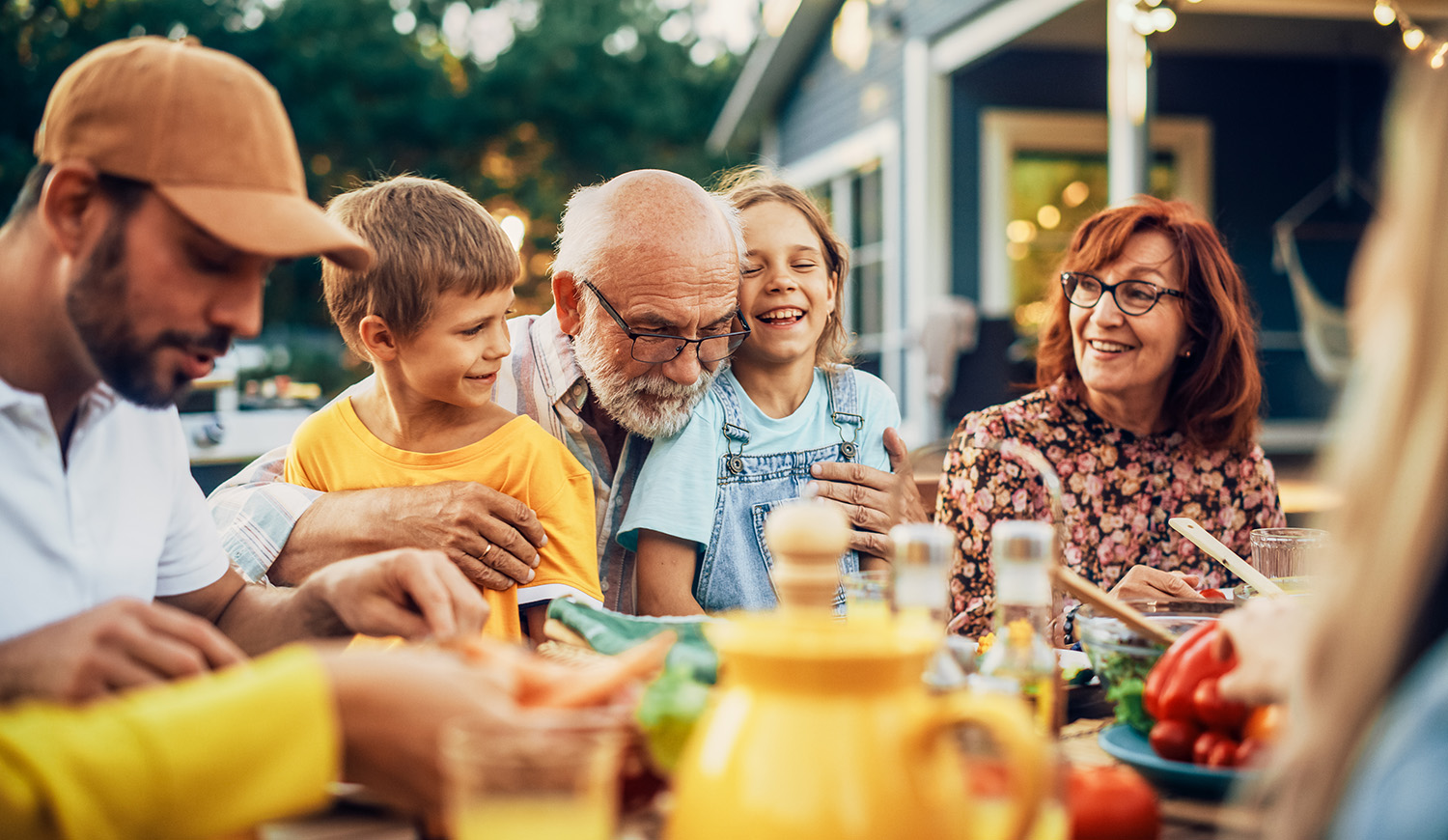 Boldog idős nagyapa az unokájával és családjával a kertben az étkezőasztalnál