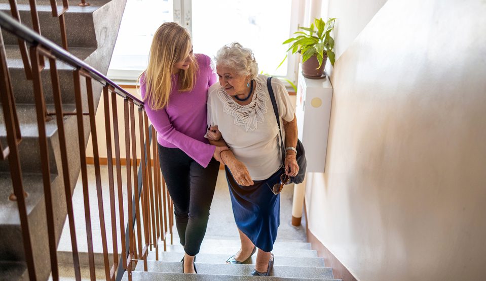 Fiatal nő segít egy idős nőnek a lépcsőn felmenni