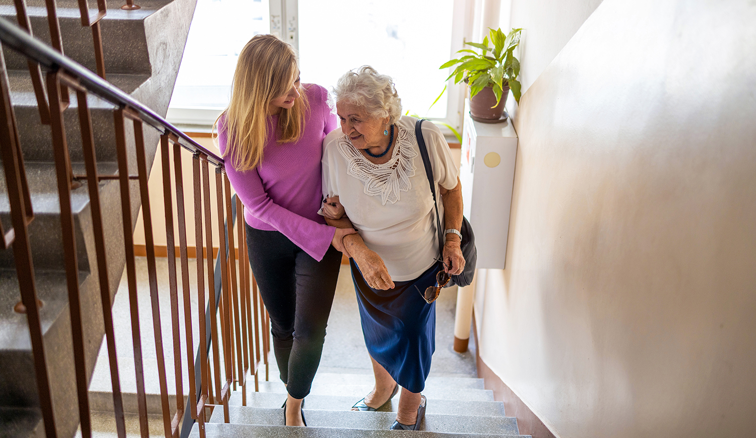 Fiatal nő segít egy idős nőnek a lépcsőn felmenni