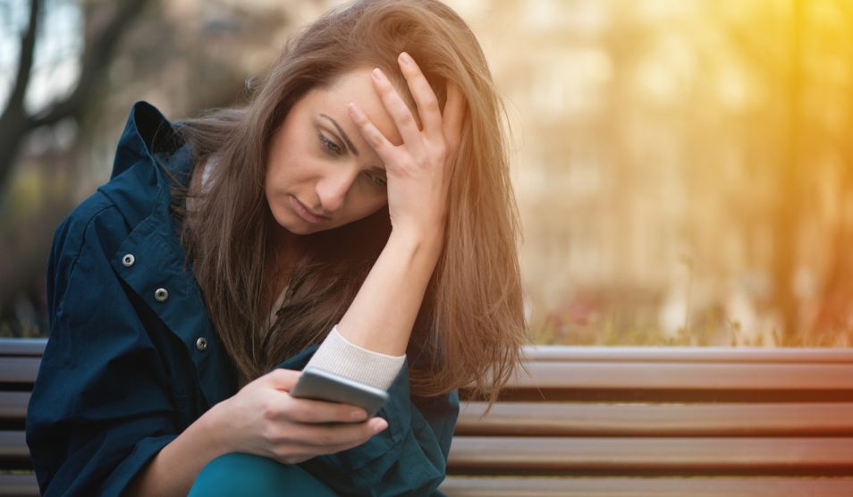 aggódó nő nézi a mobiltelefonját