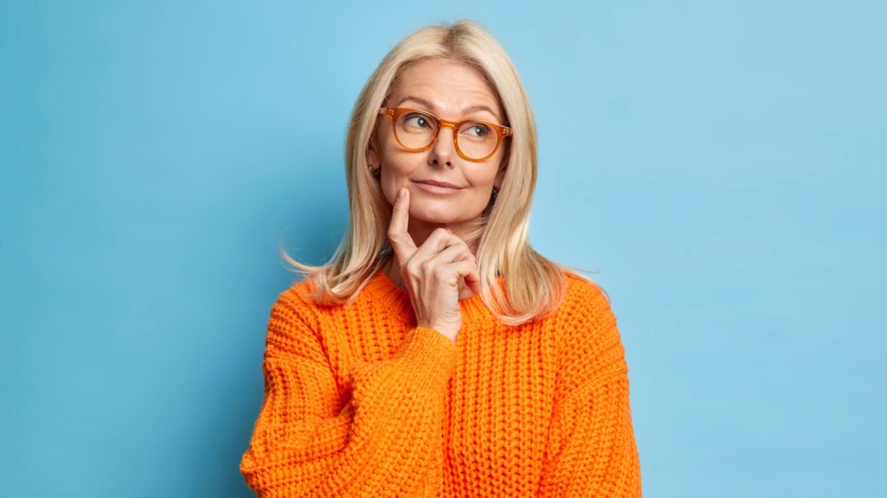 egy idős hölgy narancssárga pulóverben gondolkozik
