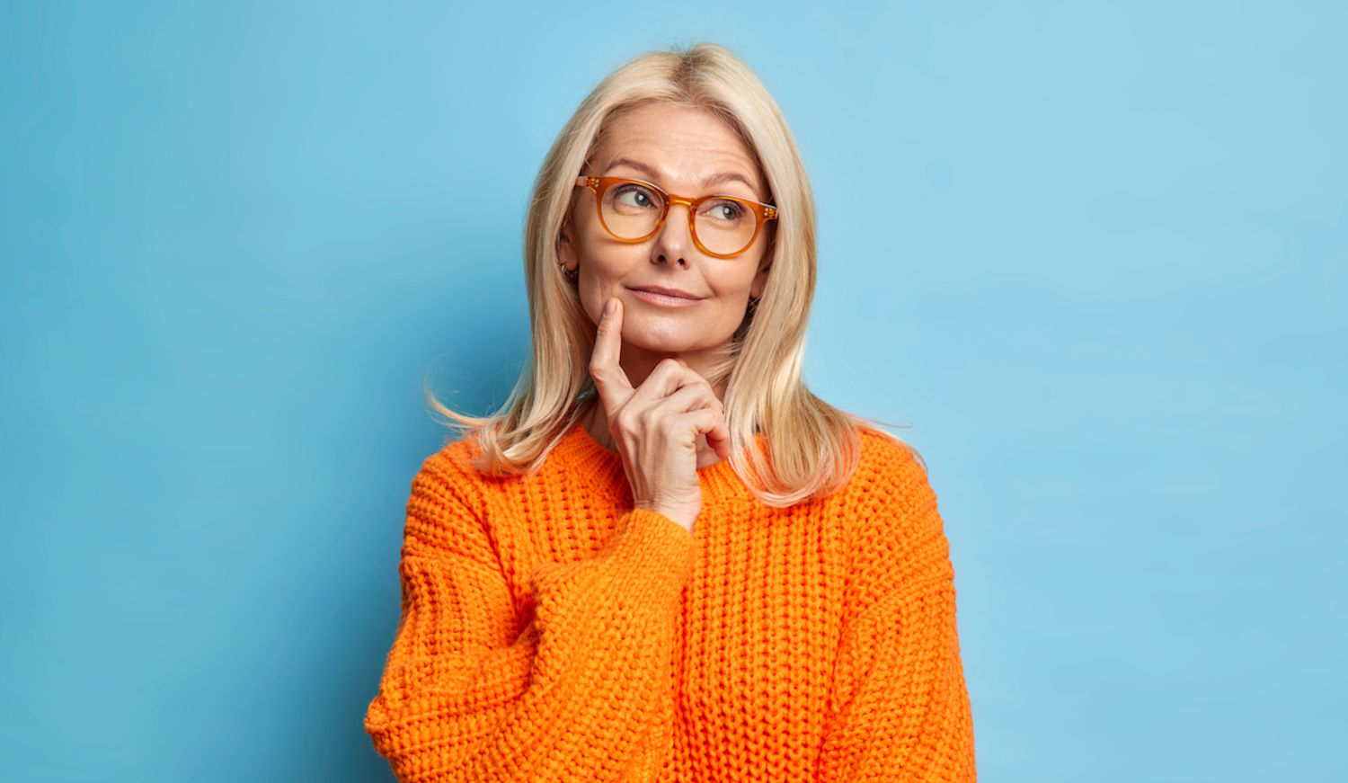 egy idős hölgy narancssárga pulóverben gondolkozik