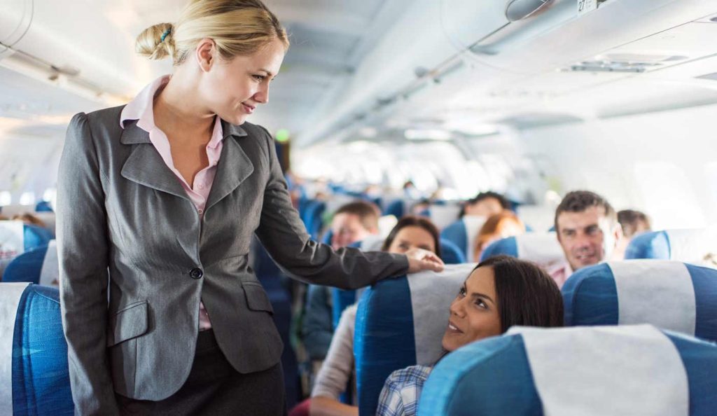 Légiutas-kísérő kedvesen mosolyog az utasokra a repülőn