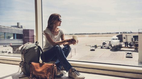 nő ül a repülőtéren kávéval a kezében, nézi a felszálló repülőket