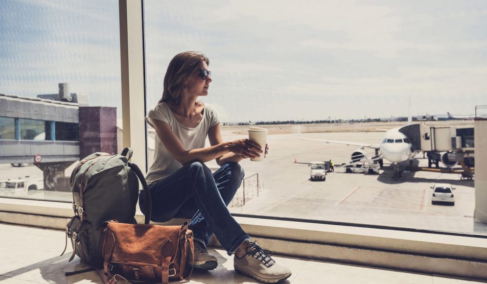 nő ül a repülőtéren kávéval a kezében, nézi a felszálló repülőket