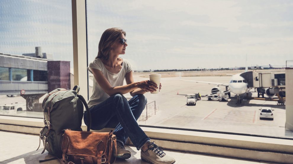 nő ül a repülőtéren kávéval a kezében, nézi a felszálló repülőket