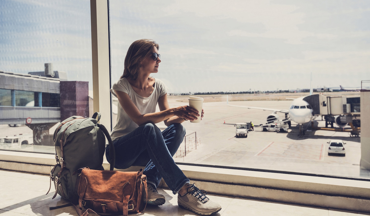 nő ül a repülőtéren kávéval a kezében, nézi a felszálló repülőket