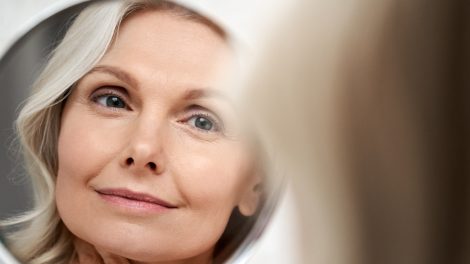 gyönyörű 50+ nő áll a tükör előtt és szépen kisminkeli magát