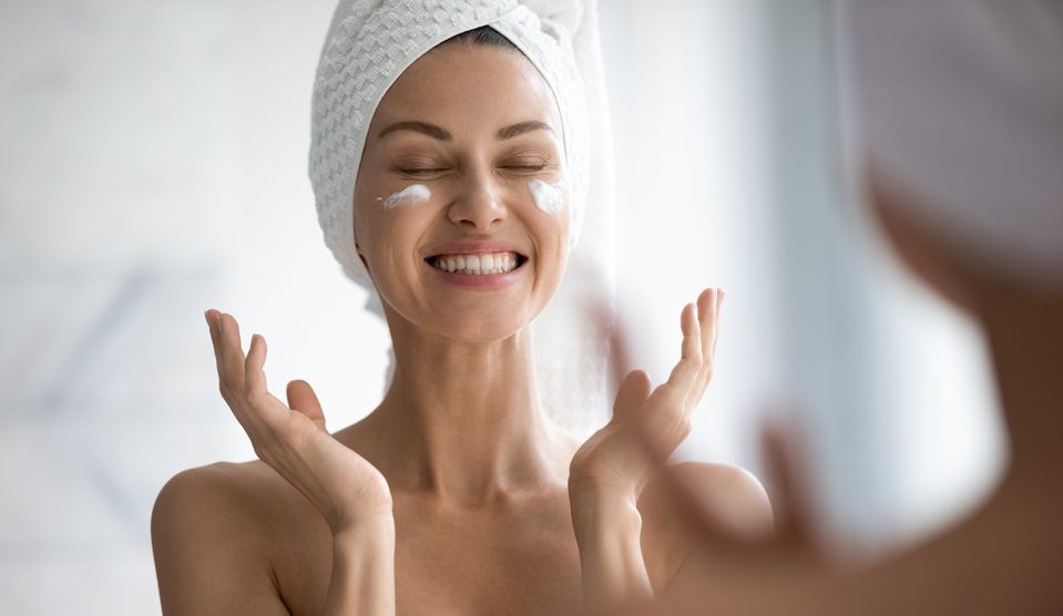 Boldog fiatal nő csukott szemmel krémezi az arcát