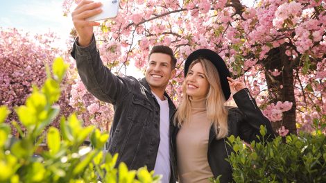 Boldog pár szelfit készít virágzó cseresznyefa alatt