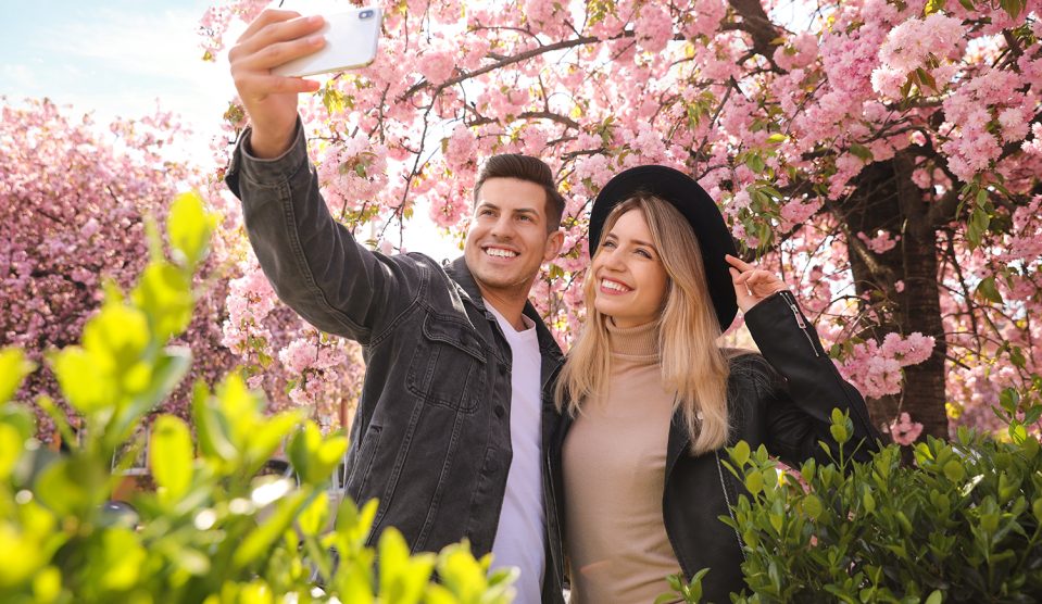 Boldog pár szelfit készít virágzó cseresznyefa alatt