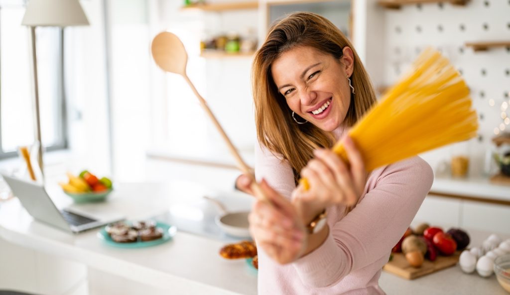 vidám fiatal háziasszony tésztát főz a konyhában