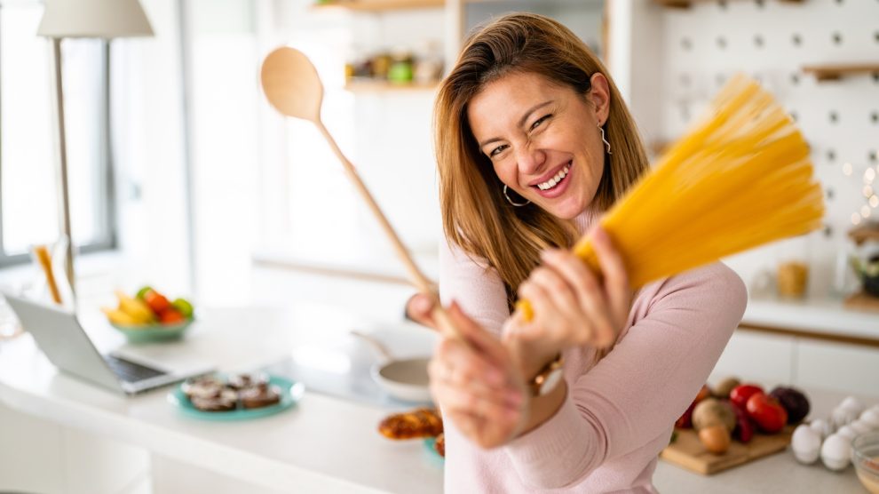 vidám fiatal háziasszony tésztát főz a konyhában