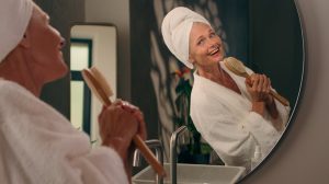 szép idős nő a fürdőszobában a tükör előtt énekel egy fésűbe