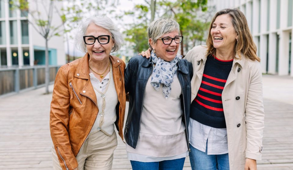 „Három nyugdíjas korú nő nevetve sétál együtt a szabadban. Hatvanas éveikben járó barátnők egy kis csoportja beszélgetve, jókedvűen élvezi egymás társaságát egy városi utcán. Az időskori barátság pillanata.”