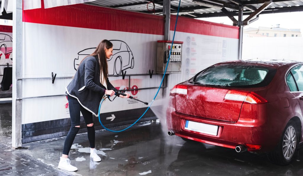 nő kézi autómosoóban mossa a piros autóját