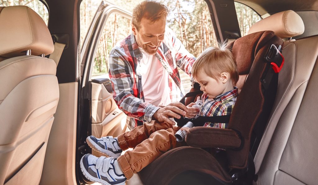apuka autós gyerekülésbe teszi be a kisfiát a kocsiban